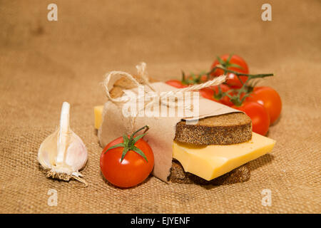 Sandwich mit Käse eingewickelt in Papier, Cherry-Tomaten und Knoblauch auf alten Tuch Stockfoto