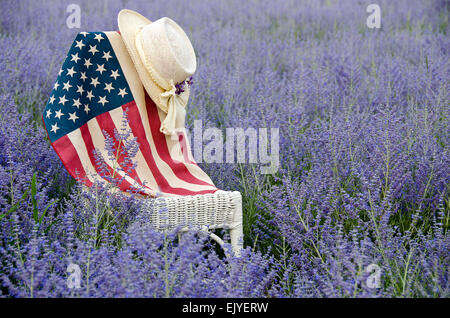 Hut und amerikanische Flagge auf einem weißen Korbstuhl in einem Feld von lila russischer Salbei. Stockfoto