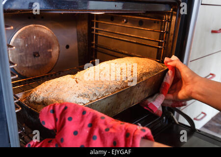 Junge Frau von hand Laib Vollkornbrot hausgemacht braun Korn aus dem heißen Ofen entfernen Stockfoto