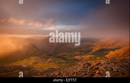 Die Sonne bricht durch die Wolken während des Abstiegs von Scafell Pike. Stockfoto