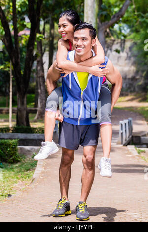 Asiatischen Mann mit seiner Freundin Piggyback für Sport in einer Pause während seiner Sport-Ausbildung Stockfoto