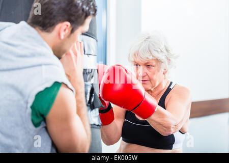 Ältere Frau mit Trainer im Boxen sparring, Sandsack schlagen Stockfoto