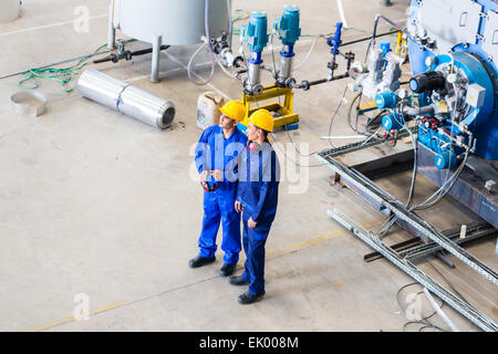 Zwei Arbeiter im Industriebetrieb diskutieren vor Maschinen, Ansicht von oben auf die Männer Stockfoto