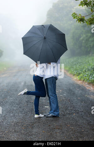romantische Pärchen versteckt sich hinter dem Schirm im Regen Stockfoto