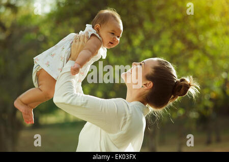 Schöne Frau hebt hoch ihre entzückende Baby Mitte Luft und schaut sie lächelnd. Glückliche Eltern verbringen Zeit mit Tochte spielen Stockfoto