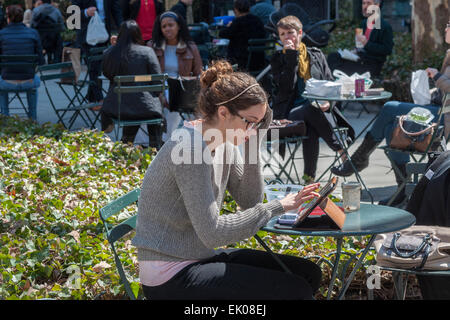 Eine Frau nutzt er das iPad, andere Park Besucher der Ausscheidung der Winterdepression im Bryant Park in New York auf Donnerstag, 2. April 2015 beitreten. Warmen Wetter in der Mitte der 60er Jahre zog Büroangestellte und Touristen im Freien. (© Richard B. Levine) Stockfoto