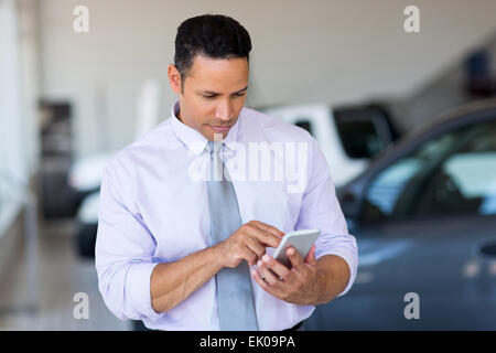 Mitte Alter Autoverkäufer mit Handy im Showroom Stockfoto