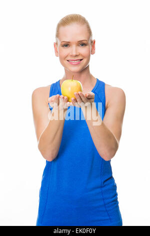 blonde lächelnde Frau trägt Fitnesskleidung und hält einen Apfel mit beiden Händen Stockfoto