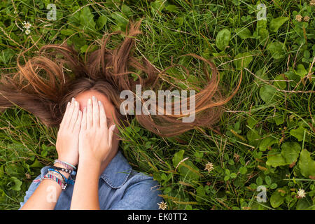 Junges Mädchen mit langen Haaren, Augen zu verschließen, liegend auf der grünen Wiese. Stockfoto