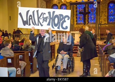 Detroit, Michigan USA - Mitglieder des Gesu katholische Kirche und die Bewohner der umliegenden Nachbarschaft kam ein Karfreitag Frieden gehen. Die Veranstaltung war eine Reaktion auf die jüngsten Dreharbeiten Bundesrichter Terrence Berg, ein Mitglied der Kirche und der Bewohner der Nachbarschaft, in einem versuchten Raub. Gesu Pastor Robert Sullin S.J führt die Prozession aus der Kirche, gefolgt von Berg in einem Rollstuhl. Bildnachweis: Jim West/Alamy Live-Nachrichten Stockfoto