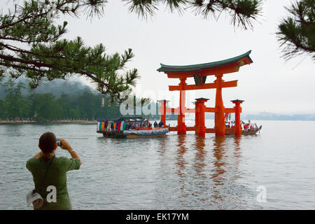 Touristen fotografieren Boot nähert sich Torii Tor des Itsukushima-Schrein während Kangen-Sai Festival, Miyajima, Japan Stockfoto