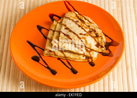 Dessert-Crêpes mit Schokosauce auf orange Teller Stockfoto