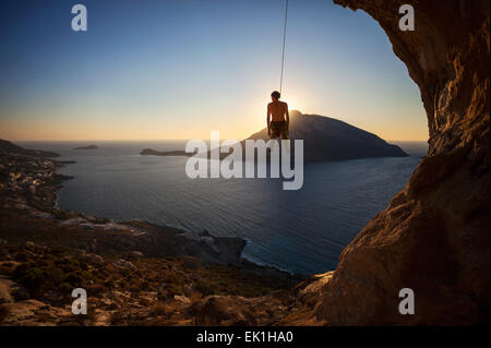 Kletterer hängen am Seil beim Vorstieg bei Sonnenuntergang mit Telendos Insel im Hintergrund Stockfoto