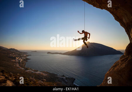 Kletterer hängen am Seil beim Vorstieg bei Sonnenuntergang mit Telendos Insel im Hintergrund Stockfoto