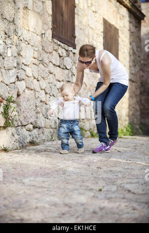 Niedliche Baby junge macht seine ersten Schritte mit Hilfe seiner Mutter Stockfoto