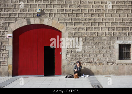 Frau sitzt auf dem Boden außerhalb Altbau, am Handy, auf einem Platz in Barcelona, Katalonien, Spanien Stockfoto