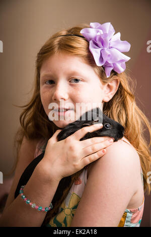 Acht - jährige Mädchen halten und kuscheln ihr Haustier Meerschweinchen auf die Schulter Stockfoto