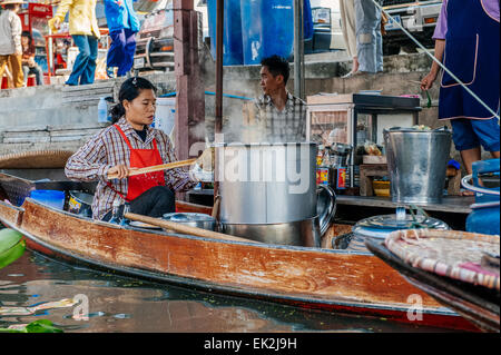 Thai Frau bereitet Essen in einem Boot auf dem schwimmenden Markt in Damnoen Saduak. Der schwimmende Markt ist eine wichtige touristische Attraktion. Stockfoto