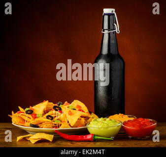 Tortillachips mit Käse, Salsa und Guacamole Dip und Flasche Bier Stockfoto