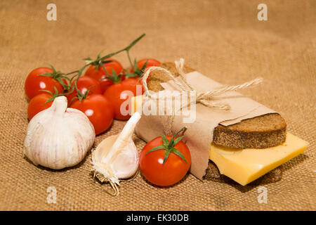 Sandwich mit Käse eingewickelt in Papier, Cherry-Tomaten und Knoblauch auf Tuch Stockfoto