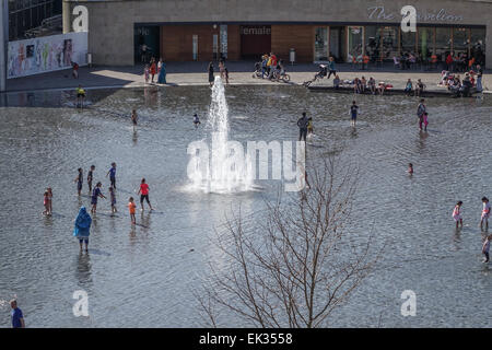 Bradford, West Yorkshire, Großbritannien, 6. April 2015. Erwachsene, Kleinkinder und Jugendliche genießen die Stadtpark mirror Pool und Brunnen im Centenary Square, Großbritanniens größte Stadtzentrum Wasserspiel. Blick vom Riesenrad. Eine glückliche multikulturelle Mischung von Menschen, Paddeln, Sonnenbaden und Spaß auf einer sonnigen Bank Ostern Montag. Bildnachweis: Mick Flynn/Alamy Live-Nachrichten Stockfoto