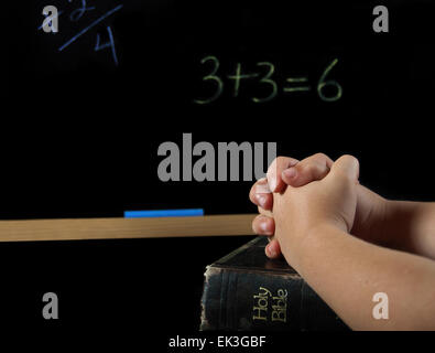 Kind die Hände gefaltet im Gebet auf die Bibel in der Schule mit Tafel. Stockfoto