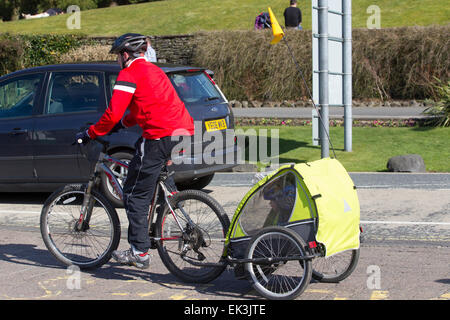 Mann im Helm Fahrradanhänger mit Kind auch tragen Fahrradhelmes innen Abschleppen Stockfoto