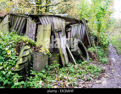 Verlassener Bauernhof Schuppen und verworfen Traktorreifen in einer bewaldeten Umgebung neben einem Schlamm-Titel Stockfoto