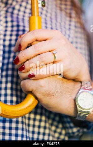 Ein Brautpaar Hände halten einen Regenschirm zusammen. Die Frau trägt einen Verlobungsring. Stockfoto