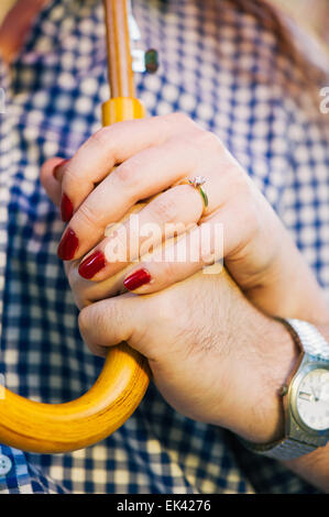 Ein Brautpaar Hände halten einen Regenschirm zusammen. Die Frau trägt einen Verlobungsring. Stockfoto
