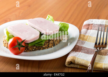 Zwei Scheiben Schinken mit Brot und Tomaten auf einem weißen Teller Stockfoto