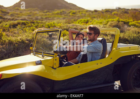 Porträt des jungen Brautpaares auf einem Roadtrip in einen Strand Buggy. Lächelnde junge Frau mit ihrem Freund, Auto zu fahren, in den Hügeln Stockfoto