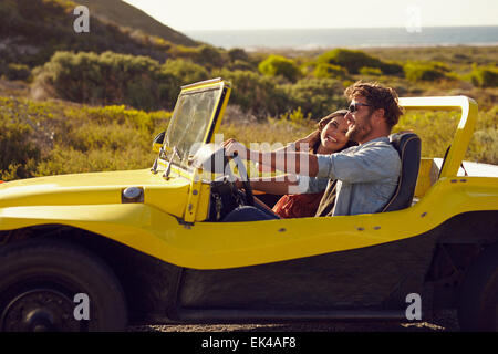 Lächelnde paar geht an Feiertagen zusammen an einem Sommertag. Junger Mann mit seiner Freundin auf Roadtrip in einem Buggy Auto. Stockfoto