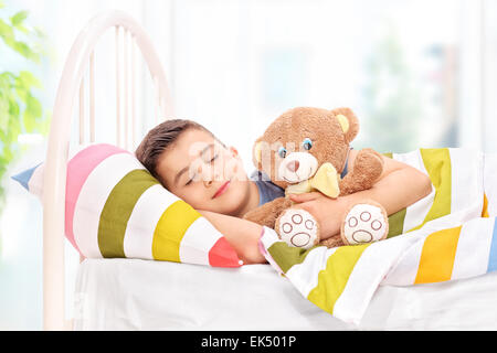 Schöne junge mit einem Teddy-Bären in einem bequemen Bett schlafen bedeckt mit einer gestreiften bunte Decke zu Hause Stockfoto