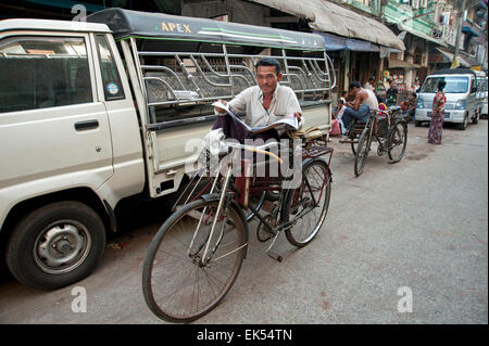 Happy burmesischen Rikscha Fahrer sieht von seiner Zeitung auf seinem rikscha taxi Yangon Myanmar sitzen Stockfoto