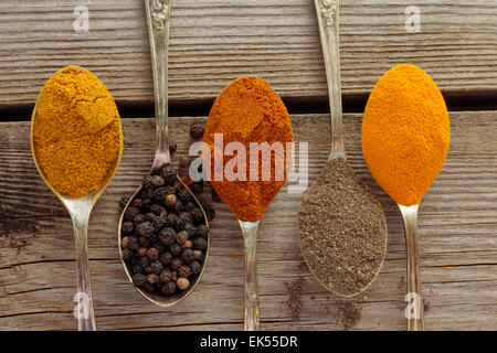 Curry, schwarze und rote Paprika, Pfeffer und Curcuma auf alten Metalllöffel Draufsicht Stockfoto