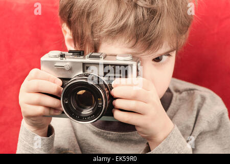 Kleines Mädchen hält Retro-Kamera und Blick durch den Sucher. Kindheit Lebensstil Moment der Kreativität und Exploration. Stockfoto