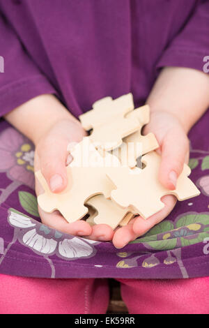 Kleines Mädchen (5 Jahre) Stücke von Holzpuzzle in ihren Händen hält. Konzeptbild von Kindheit Herausforderung, Zusammenarbeit und Stockfoto