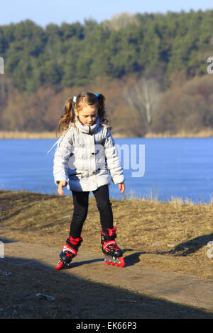 junges schönes Mädchen geht in Inline Skates auf dem Boden Stockfoto