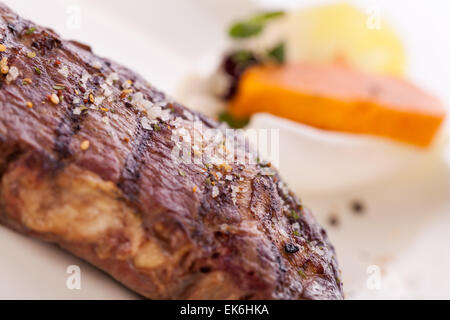 Lecker gegrilltes Rindersteak mit einem gezwirbelten Stück Butter und ein Zweig frischer Rosmarin garniert und serviert auf einem weißen Teller, enge u Stockfoto