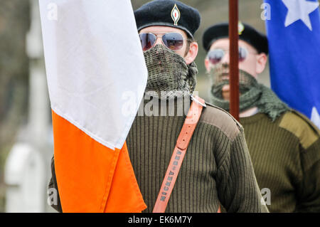 Männer, gekleidet in Irischen paramilitärischen Uniformen, deren Gesichter vom Militärischen scrim Schals erfassten Irische Flaggen in Milltown Friedhof, während der Hauptversammlung Stockfoto