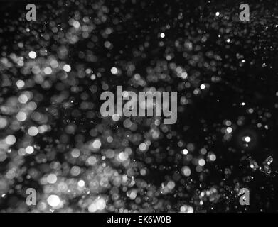 Bokeh leuchtet auf schwarzem Hintergrund, defokussierten Schuss von Wassertropfen in der Luft schwebend fliegen Stockfoto