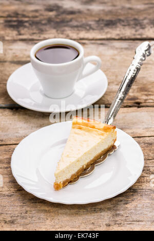 Stück Käsekuchen auf Teller mit Tasse Kaffee am Tisch aus Holz. Restaurant Dessert Menühintergrund Stockfoto