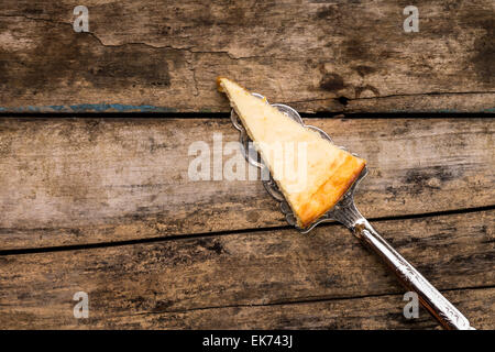 Stück New Yorkkäsekuchen auf Schönheit Tortenheber auf alten Holztisch. Restaurant Dessert Menühintergrund. Stockfoto