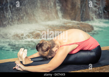 Frau Yoga zu praktizieren in der Nähe von Wasserfall. Sitzen nach vorne falten. Paschimottanasana Stockfoto