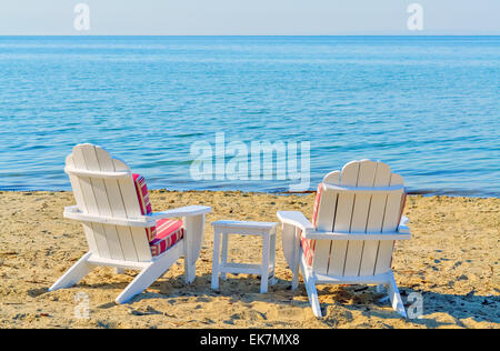 Zwei leere weiße Sessel am Strand neben dem türkisfarbenen Meer Stockfoto