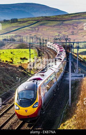 Stromleitungen und Portale, Elektrozüge in Cumbria, Großbritannien 8th. April 2015. Wetter in Großbritannien. Strahlender sonniger Tag über den Cambrian Fells und der Westküste mit dem Bahnverkehr der Carlisle Line. Die Baureihe 390 Pendolino ist ein elektrischer Hochgeschwindigkeitszug, der von Virgin Trains im Vereinigten Königreich betrieben wird. Es handelt sich um elektrische Triebzüge, die die Pendolino-Technologie von Fiat Ferroviaria verwenden und von Alstom gebaut wurden. Ursprünglich wurden zwischen 2001 und 2004 53 9-Auto-Einheiten für den Betrieb auf der West Coast Main Line (WCML) gebaut, weitere vier Züge und 62 Autos wurden zwischen 2009 und 2012 gebaut. Stockfoto