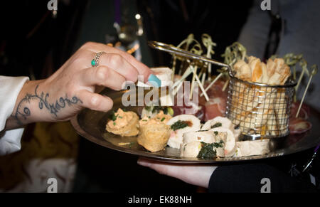 Frau mit tätowierte Hand und lange Aqua Nägel unter Canapé aus einem Tablett serviert wird. Unter anderem gefüllte Hähnchen und Speck Oliven. Stockfoto