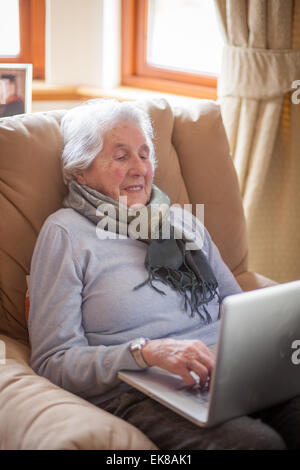 Alte Dame sitzt im Sessel mit einem Laptop. Stockfoto