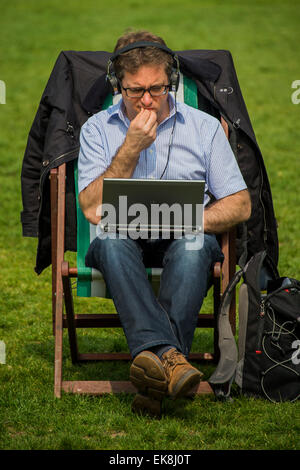 London, UK. 8. April 2015. Ein Mann konzentriert sich auf seinem Laptop. Die Frühlingssonne bringt Arbeitnehmer und Touristen um die Mittagszeit. Sie genießen in den Liegestühlen entspannen oder auch die Verwendung als Outdoor-Büros. Green Park, London, 8. April 2015. Bildnachweis: Guy Bell/Alamy Live-Nachrichten Stockfoto